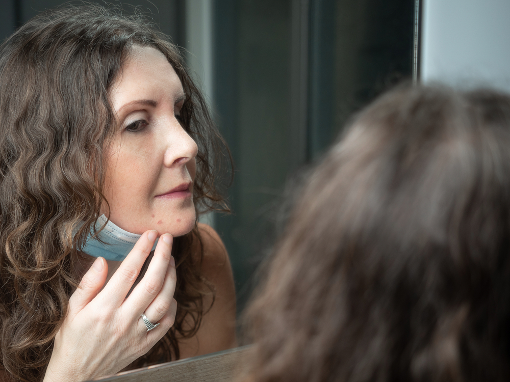 A middle aged women looks into the mirror and inspects her face and lip